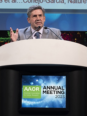 Jose Conejo-Garcia, MD, PhD, speaks from a podium that displays the logo of the AACR Annual Meeting 2023