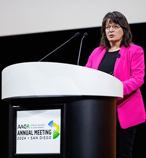 Kornelia Polyak, MD, PhD, FAACR, at a podium on stage during the plenary "Discovery Science in Early Cancer Biology and Interception" at the AACR Annual Meeting 2024.