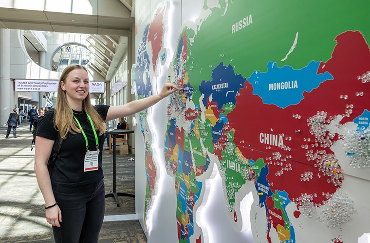 A woman at the AACR Annual Meeting 2024 placing a pin on the map of the world to show where she came from.