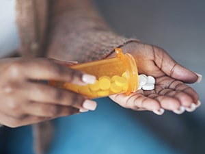 Person pouring medication out of pill bottle into hand.